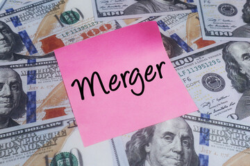 Pink sticky note with MERGER text over US dollar bills. Concept of corporate acquisition and business strategy.