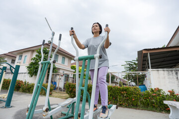 A woman exercising on outdoor fitness equipment in a village park, promoting a healthy lifestyle, daily workout routine, physical activity, community wellness, active living.