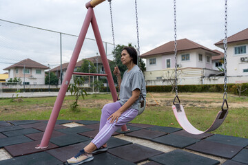A woman relaxing on a swing in a quiet village park, enjoying outdoor leisure, fresh air, and peaceful surroundings, representing wellness, slow living, community lifestyle, nature-focused relaxation.