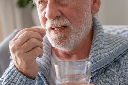 Senior man takes pill with glass of water in hand. Stressed elderly bearded man drinking sedated antidepressant meds. Man feels depressed, taking drugs. Medicines at work