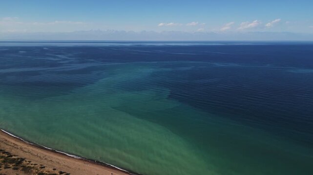 Aerial view of white tents nestled between the azure waters of the lake and the rugged, sun-drenched mountains, Ak Say, Issyk-Kul Region, Kyrgyzstan