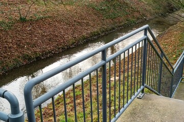 Concrete stairs with metal railing next to canal in autumn