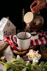 Hands pouring hot drink into mug with marshmallows. Cozy winter preparation moment and festive home lifestyle scene.