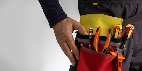 Electrician in uniform with tool belt with various instruments.  Space for text, closeup.