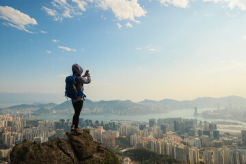 Successful woman hiker stand on the cliff edge taking selfie with smartphone in hong kong