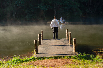 Tourists stand on a wooden bridge, gazing at the sea of ​​mist rising above the surface of Pang Ung Lake in Mae Hong Son Province, northern Thailand.