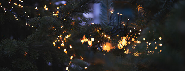 Horizontal close-up of a christmas tree with golden bokeh lights.