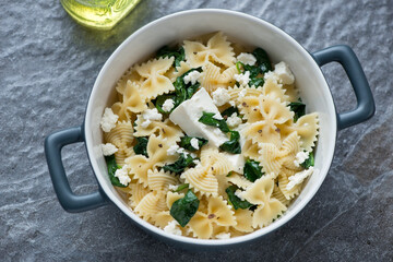 Serving pan with farfalle, wilted spinach and feta, horizontal shot on a dark-grey granite background, elevated view