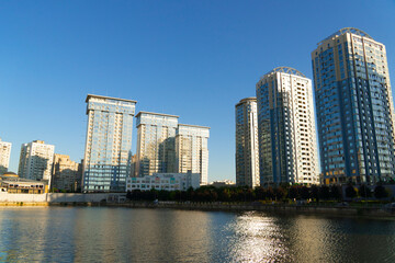 Naklejka premium A complex of modern multi-story apartment buildings standing on the shore of a lake. Urban architecture and city landscape in the evening sun