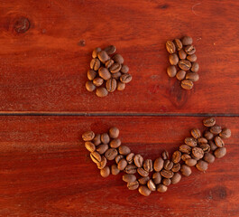 Smiley face made of roasted coffee beans on a rustic dark wooden surface