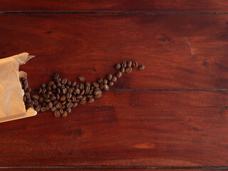 Roasted coffee beans spilling from a paper bag on a rustic dark wooden background with copy space