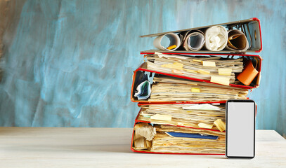 Messy file folders, ring binders grungy paperwork.Red tape, bureaucracy, overworked, beat the clock business concept smartphone with blank screen.