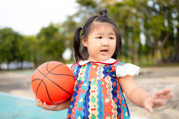A cute little Asian girl stands holding a basketball on an outdoor court,A girl child in sportswear playing basketball game