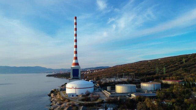 Aerial view of Urinj Thermal Power Plant on the Croatian Adriatic coast near Rijeka. Industrial architecture meets stunning natural landscape under a clear winter sky.