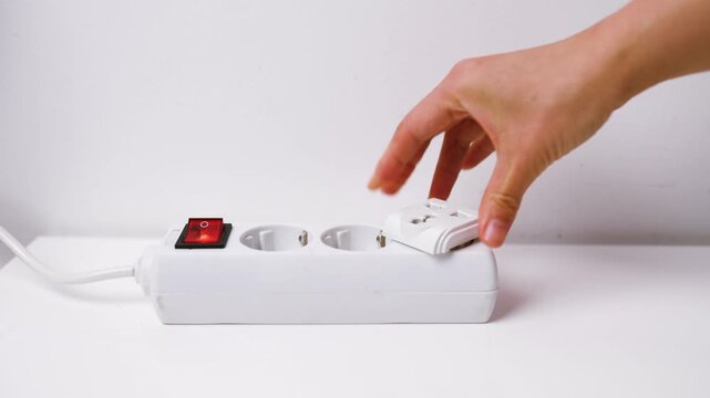 Close-up of female hand plugging a plug into a multiple socket