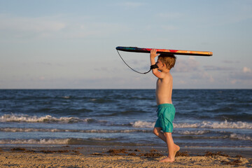 Young boy walking down beach with boogie / skim board
