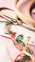 Sewing tools and colorful threads arranged on a pink background for creative crafting projects