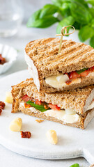 Delicious whole grain sandwich with fresh vegetables and creamy cheese on a marble cutting board