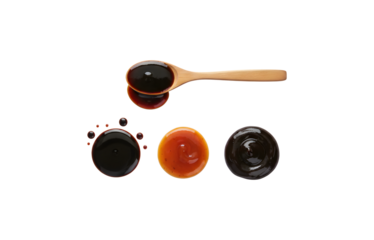Soy sauce, teriyaki sauce, oyster sauce, or balsamic vinegar puddles spilled on a wooden spoon, seen from above against a white background.
