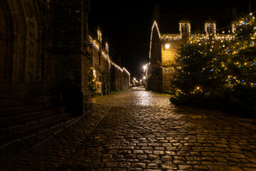 Rue pav&eacute;e du village de Locronan en Bretagne d&eacute;cor&eacute;e de guirlandes lumineuses pour les f&ecirc;tes de No&euml;l, fa&ccedil;ades en pierre &eacute;clair&eacute;es et ambiance nocturne chaleureuse.
