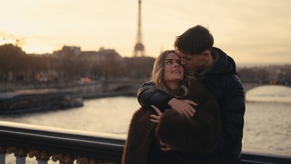 A romantic couple embraces in Paris France with the Eiffel Tower visible in the background at...