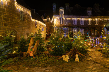 Place du village de Locronan en Bretagne d&eacute;cor&eacute;e pour les f&ecirc;tes de No&euml;l, sapins et &eacute;l&eacute;ments lumineux install&eacute;s devant les fa&ccedil;ades en pierre, ambiance nocturne festive et chaleureuse.