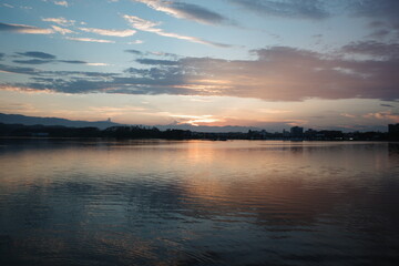 Fototapeta premium Peaceful sunset over a calm lake with silhouette of mountains and clouds reflected in water.