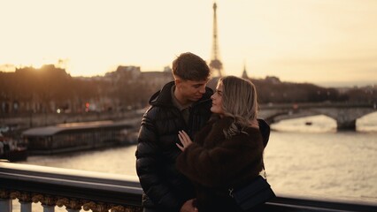 A romantic couple embraces with the Eiffel Tower in the background in Paris France at sunset. This image captures love and affection in an urban city landscape and is suitable for travel and tourism r