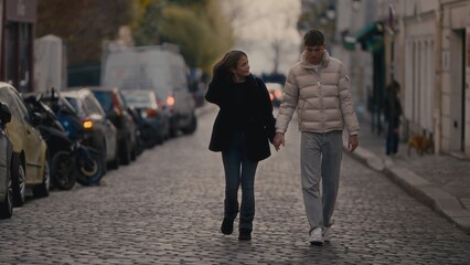 A romantic couple walks hand-in-hand down a cobblestone street in Paris France during the autumn...