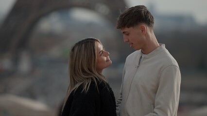 A young couple in Paris France gazes lovingly at each other with the Eiffel Tower blurred in the background. This image is perfect for illustrating themes of love travel and European vacations. © 4kclips