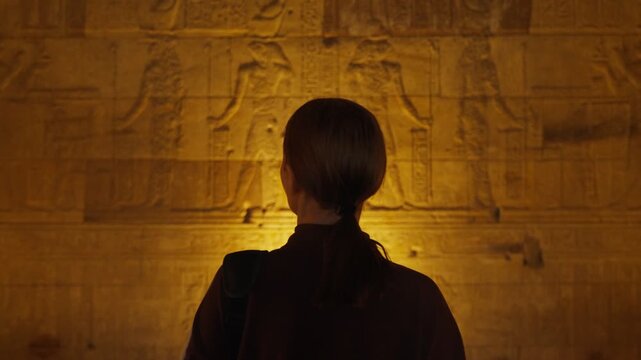 A female tourist admires the interior of the temple in Dendera or the temple of Hathor in Egypt. Ancient hieroglyphic carvings on the temple walls. The history of Egypt.