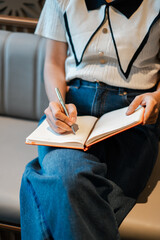A woman in casual attire writes in a notebook while seated on a sofa, capturing a moment of...