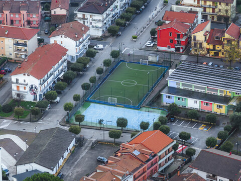Aerial view of a vibrant green football field bordered by neat rows of trees and colourful buildings, nestled in an urban landscape, San Michele di Serino, Campania, Italy.