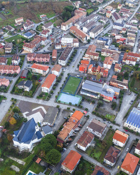 Aerial view of a church spire piercing the skyline amidst a tapestry of terracotta roofs and green spaces, a vibrant tableau of urban life unfolds below, San Michele di Serino, Campania, Italy.
