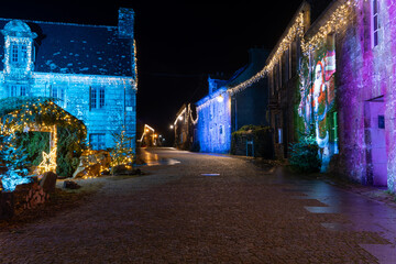 Rue pav&eacute;e du village de Locronan en Bretagne d&eacute;cor&eacute;e pour les f&ecirc;tes de No&euml;l, fa&ccedil;ades en pierre illumin&eacute;es et projection festive cr&eacute;ant une ambiance nocturne chaleureuse et authentique.