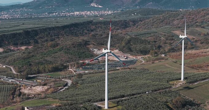 Aerial view of wind turbines standing tall amidst expansive green fields, creating a captivating contrast against the rolling hills, Serre, Campania, Italy.