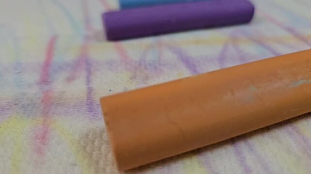 Extreme close-up of colorful pastel chalks being placed on a textured paper with artistic scribbles and blurred background.