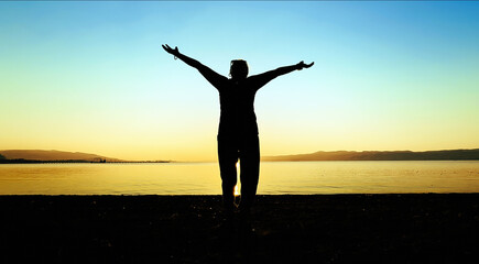 Person With Open Arms Facing Sunset Over Water at Sunset