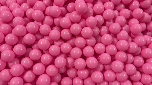 Extreme close up video of glossy pink balls packed tightly together creating a smooth abstract texture with playful tone and modern visual atmosphere

