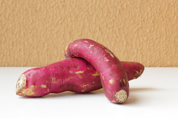 Two raw sweet potatos on white table. Horizontal food shot with copy space, perfect for healthy eating, nutrition education, organic food marketing, agriculture content, and vegetarian lifestyle.