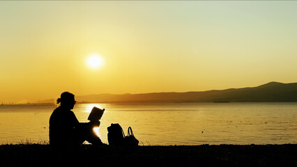 Woman Watching Sunset And Reading Book By The Sea