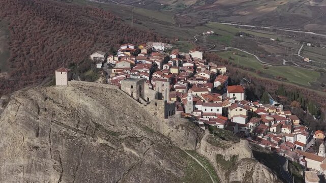 Aerial view of buildings with red roofs clinging to a rock formation, creating a striking contrast against the green landscape, Brindisi Montagna, Basilicata, Italy.