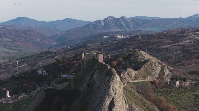 Aerial view of the ancient castle perched atop a craggy hill amidst rolling hills, its stone walls contrasting with the lush greenery, Brindisi Montagna, Basilicata, Italy.