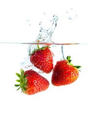 Three Ripe Strawberries Splashing into Clear Water with Bubbles on White Background