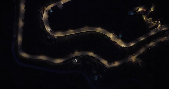 Aerial view of winding roads illuminated by streetlights cutting through the darkness, creating a stark contrast of light and shadow, Castelmezzano, Basilicata, Italy.