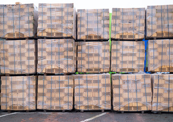 Large stacks of yellow facing bricks wrapped in protective plastic film on wooden pallets at a construction site or warehouse.