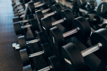 Obraz premium Close-up of professional dumbbells on a rack in a modern gym with a blurred fitness center background. 