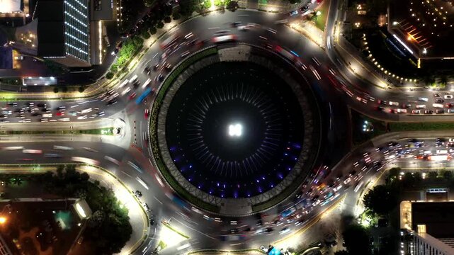 Aerial top-down hyperlapse of busy evening traffic flowing through the iconic Selamat Datang (Welcome) Monument roundabout in the central business district in Jakarta, Indonesia
