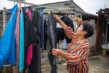 Obraz premium Elderly woman checking clothes on an outdoor drying rack, representing household chores, independence, and everyday senior lifestyle.