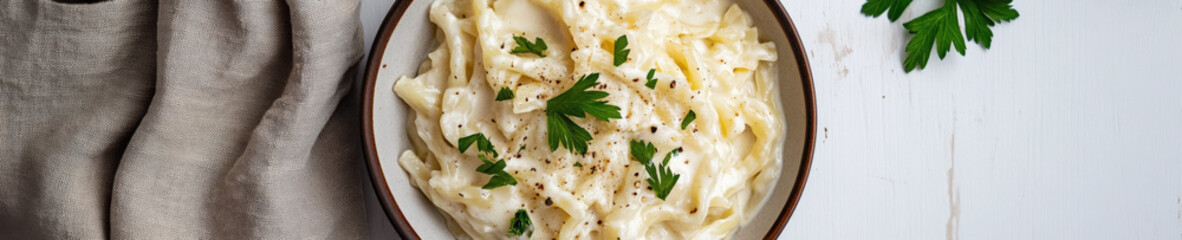 Creamy fettuccine alfredo in bowl on white wooden table banner

